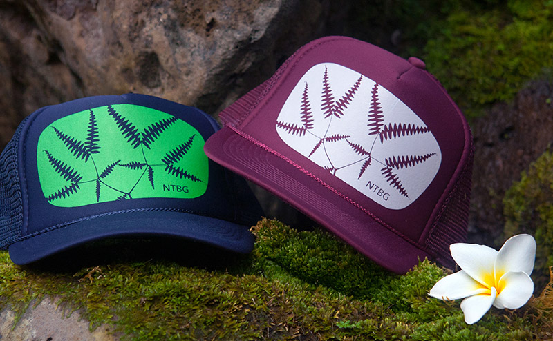 Navy and maroon trucker hats screenprinted with motif, resting on mossy rocks.